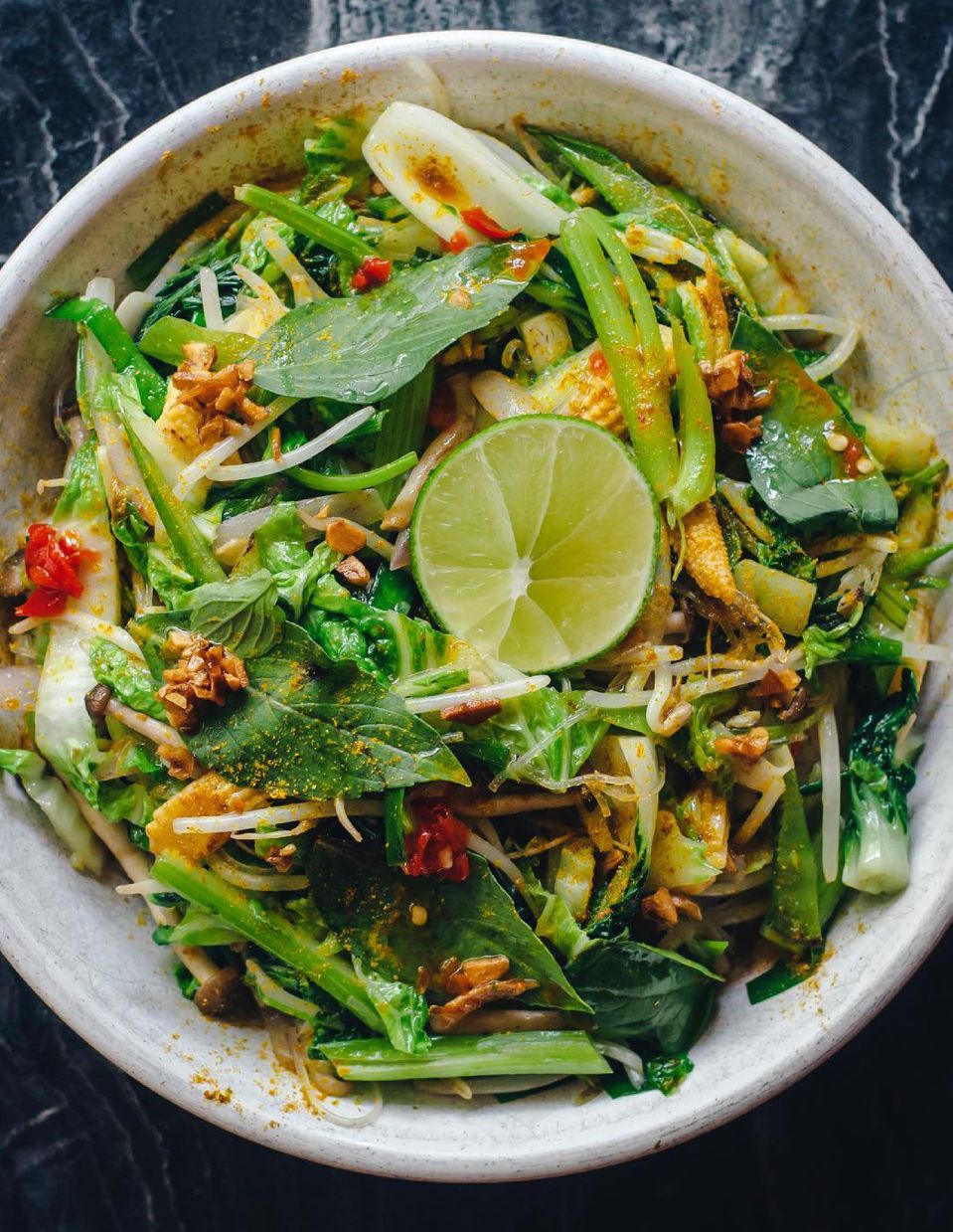 Bowl of dark leafy green, colorful veggies, and nuts representing plant-based eating.