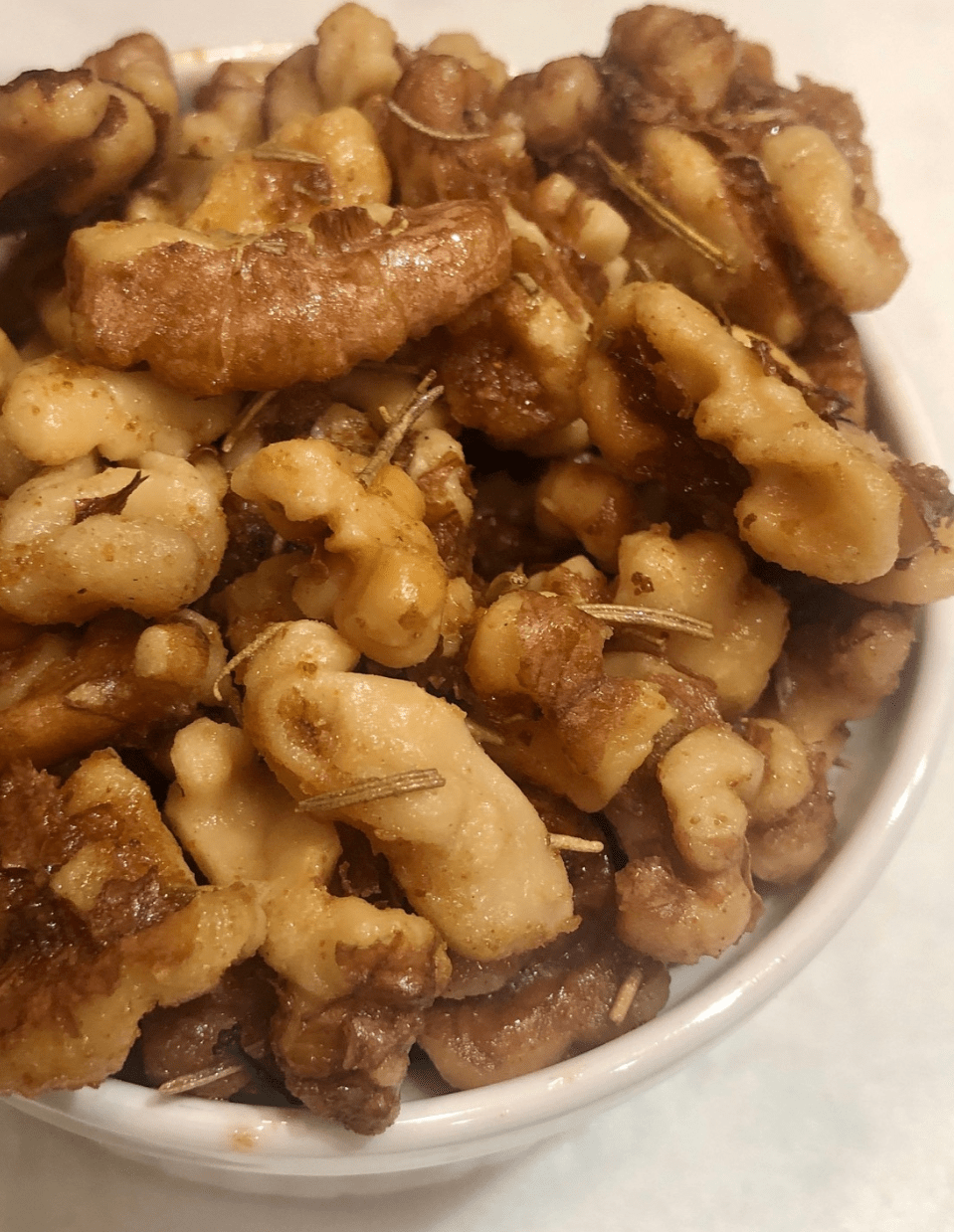 Rosemary walnuts in a small bowl, featuring crispy, flavorful walnuts with a hint of rosemary, perfect for a healthy vegan snack or topping.