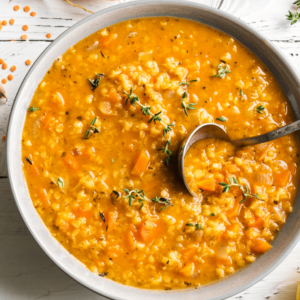 A bowl of smoky red lentil soup with carrots, spinach, and a rich broth, showcasing a hearty, vegan, and anti-inflammatory meal option.