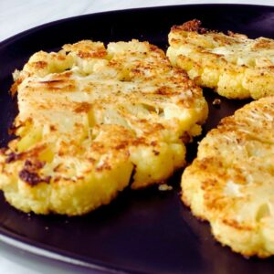 A plate of golden-brown oven-roasted cauliflower steaks garnished with a sprinkle of paprika and garlic.