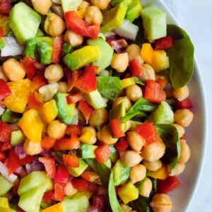 A bowl of colorful chickpea salad drizzled with Tangy Tahini Dressing, garnished with fresh greens, perfect for a healthy meal.