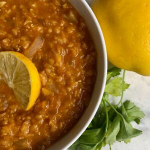 A bowl of hearty red lentil soup garnished with fresh parsley and lemon zest.