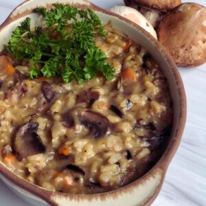 Mushroom Soup made with hearty portobello mushrooms and gourmet wild rice served in a handcrafted Gail Pittman Alfresco bowl with a garnish of fresh herbs, and baby portobellos set to the side.