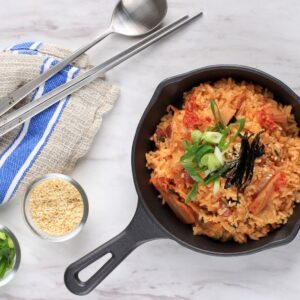 Kimchi fried rice served in a black iron skillet, garnished with strips of seaweed, sliced green onions, and sesame seeds.