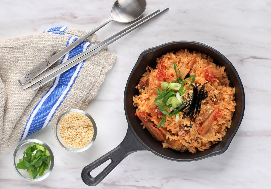 Kimchi fried rice served in a black iron skillet, garnished with strips of seaweed, sliced green onions, and sesame seeds.