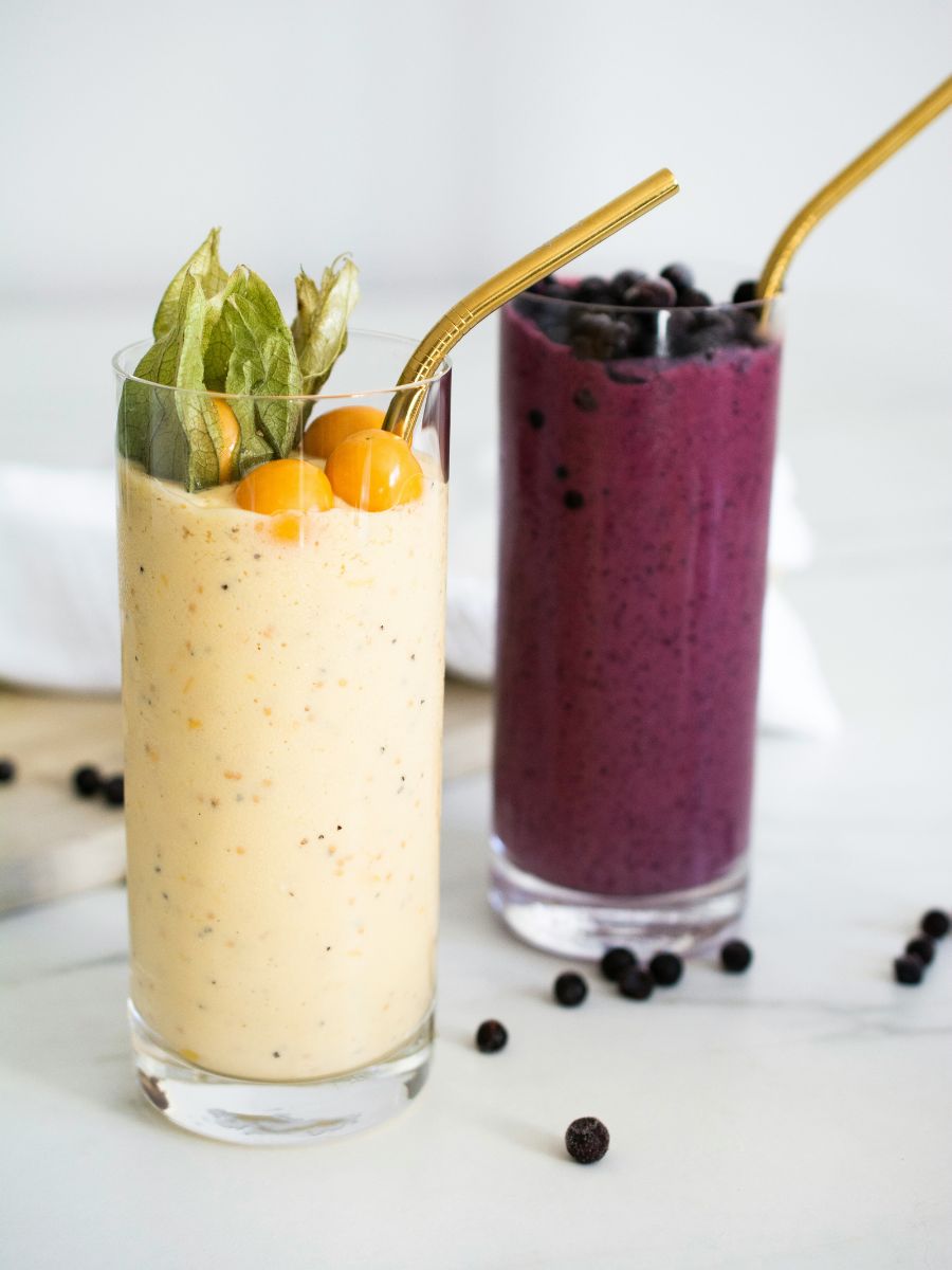 A vibrant, healthy citrus smoothie in the foreground garnished with an orange slice, with a wild blueberry citrus smoothie in the background.
