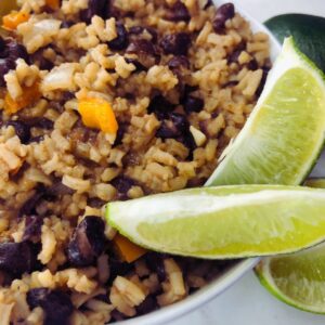 A plate of Cuban black beans served over white rice, garnished with fresh cilantro and lime wedges for a vibrant and nutritious meal.