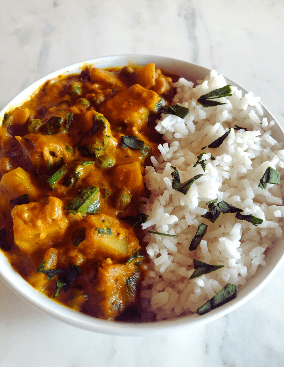 A bowl of healthy lentil potato curry garnished with fresh herbs, served over steamed rice.