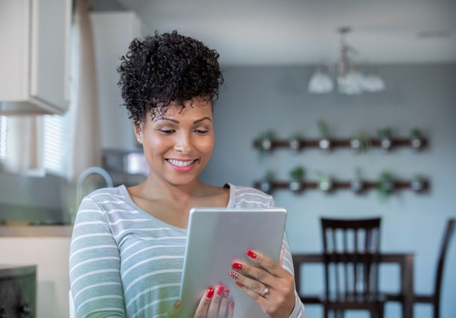 Woman standing in kitchen holding ipad during a telehealth nutrition counseling session receiving personalized dietary advice.