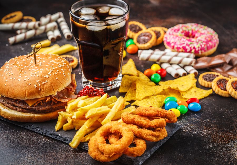 Fast food, potato chips, candy, and doughnuts on a table, illustrating a variety of ultra-processed foods often linked to health risks like obesity and diabetes.