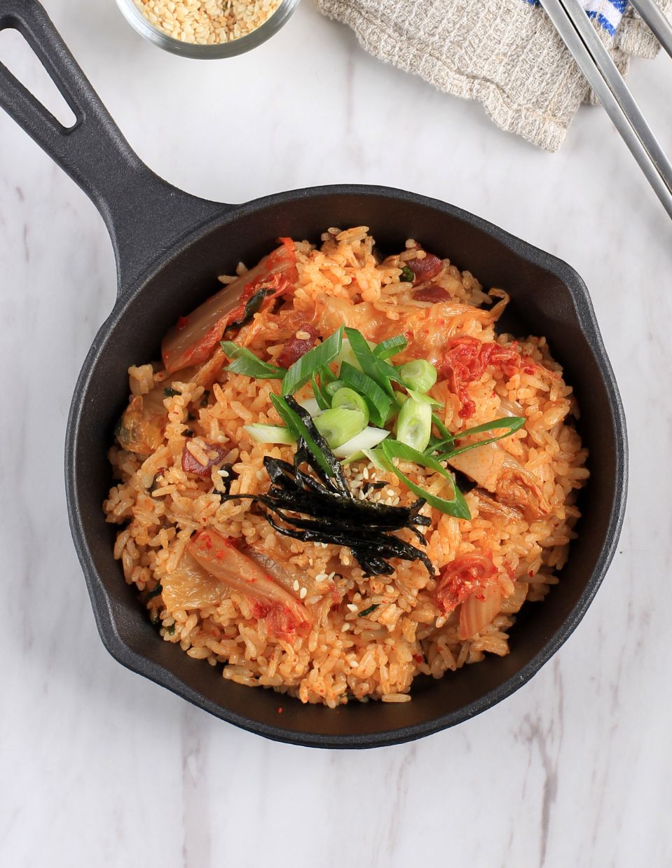 Kimchi fried rice served in a black iron skillet, garnished with strips of seaweed, sliced green onions, and sesame seeds.