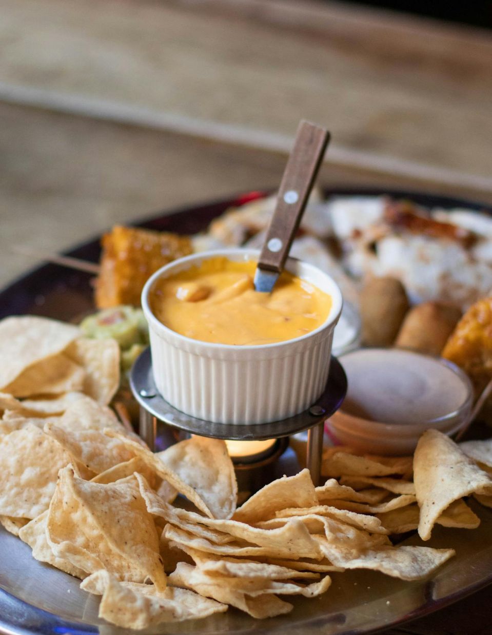 A creamy vegan nacho cheese dip in a bowl, placed on a tray alongside tortilla chips and a variety of healthy appetizers.