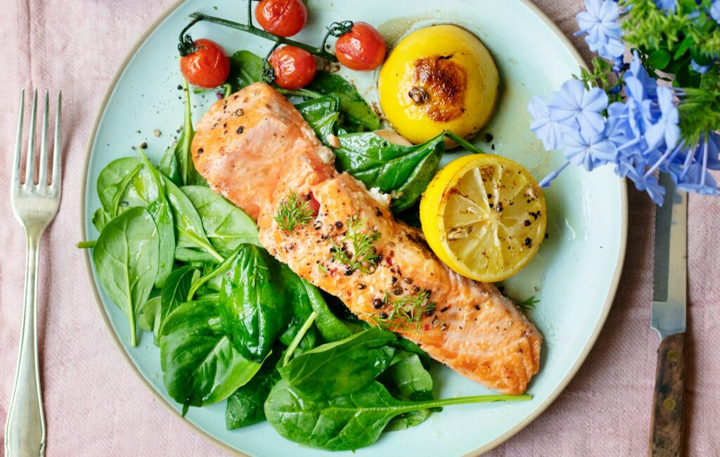 Immune boosting plate of salmon, greens, lemon, and tomatoes full of nutrients to keep you from getting sick.