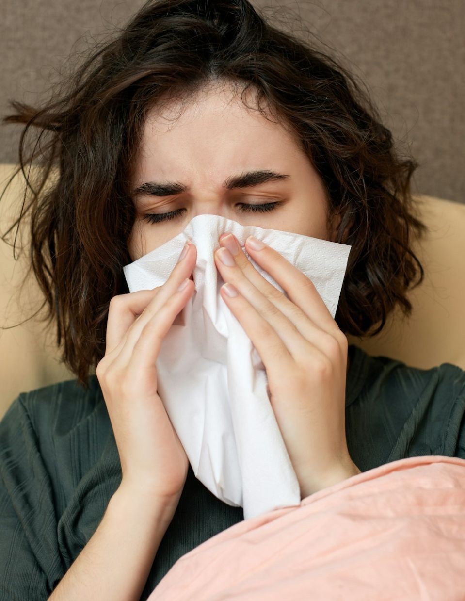 A woman in bed blowing her nose with a tissue, highlighting the importance of immune health as part of an article about preventing sickness with 10 superfoods.