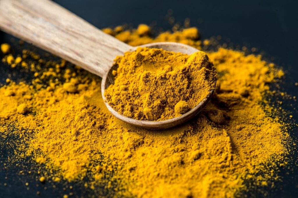 A yellow turmeric powder in a wooden spoon, a powerful spice rich in curcumin, known for its anti-inflammatory and immune-boosting properties to help keep you from getting sick.