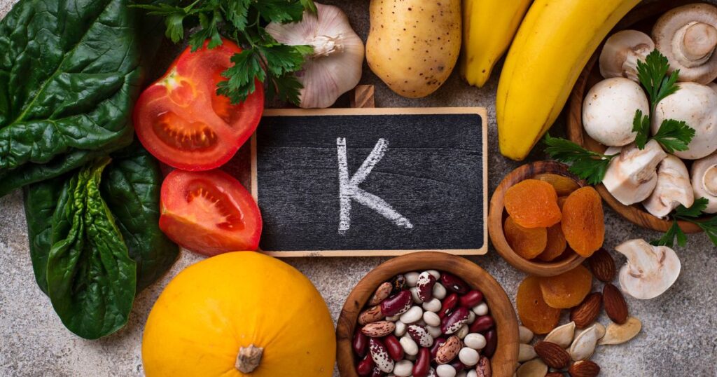 An assortment of potassium-rich foods, including bananas, sweet potatoes, avocados, spinach, white beans, and oranges, arranged on a wooden surface. These foods are known for supporting heart health, muscle function, and overall well-being due to their high potassium content.