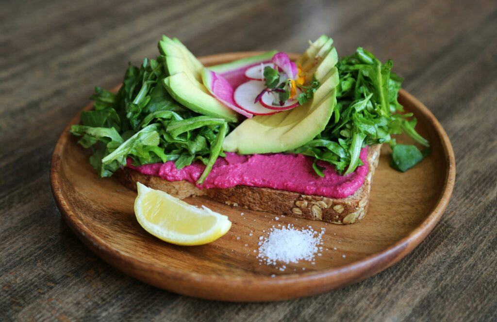 Beet hummus spread on whole wheat bread, garnished with nitrate-rich spinach and radishes for a heart-healthy snack.