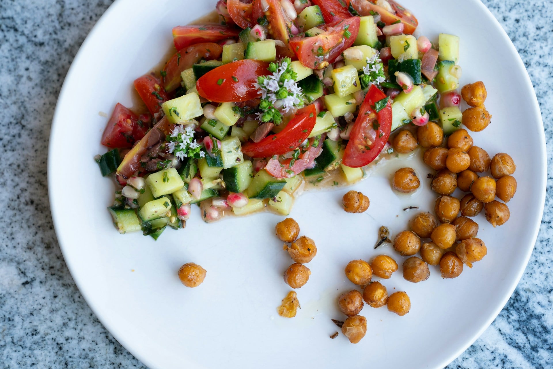 High protein Greek Chickpea Salad served on a plate with chickpeas, cucumbers, cherry tomatoes, red onion, topped with a lemon-herb dressing.