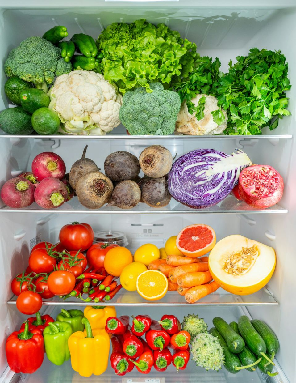 Open refrigerator filled with colorful functional foods, including fresh vegetables like leafy greens, bell peppers, pomegranates, and carrots to support heart health.