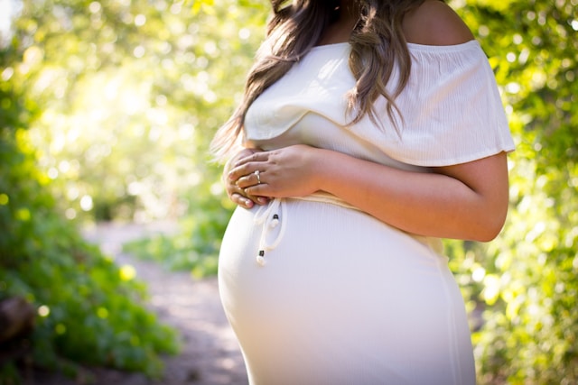 Pregnant woman in a white dress cradling her belly outdoors, surrounded by greenery and sunlight – symbolizing prenatal health, pregnancy nutrition, and maternal wellness.