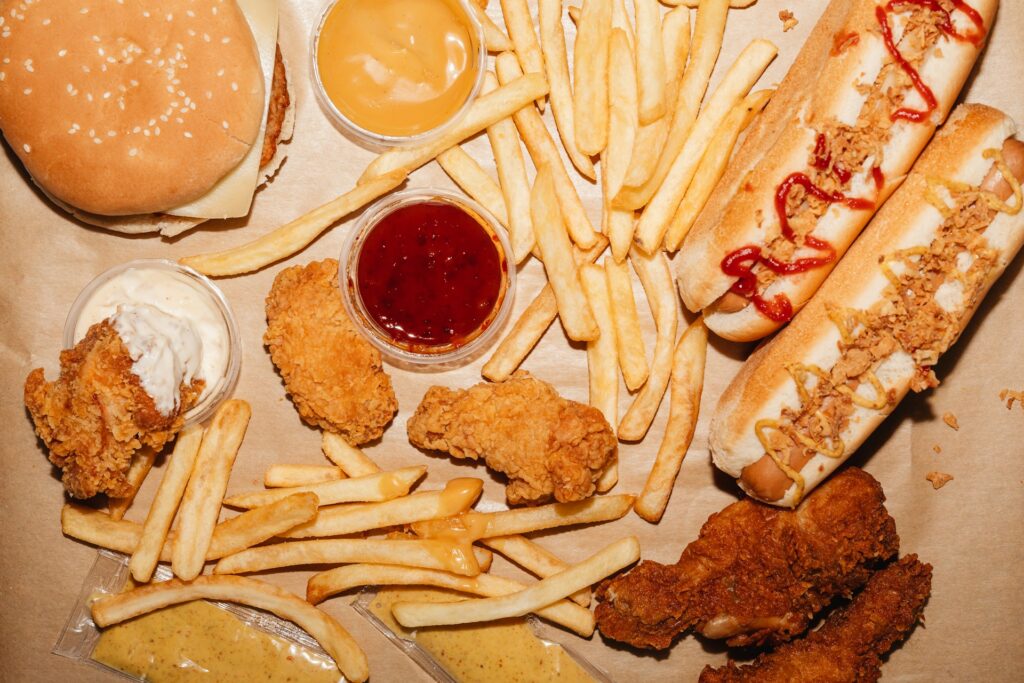 Highly processed foods such as fried chicken tenders, french fries, hot dogs, and a hamburger depicting the typical western diet that lacks food diversity.